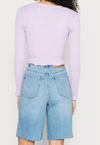 Světle fialový žebrovaný svetr s dlouhým rukávem a vlnitým lemem, spárovaný s vysokými světle modrými džínovými šortkami, které mají dvě zadní kapsy.
