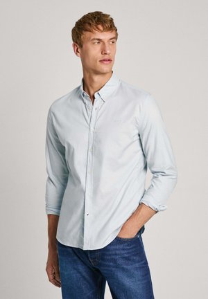 Camicia azzurra in cotone con collo, maniche lunghe e un logo discreto sul petto. Indossata con jeans blu.