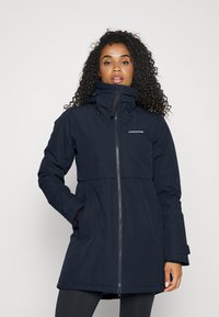 Veste imperméable bleu marine foncé avec un col haut, fermeture éclair et deux poches latérales. Présente une taille cintrée et des manches longues.