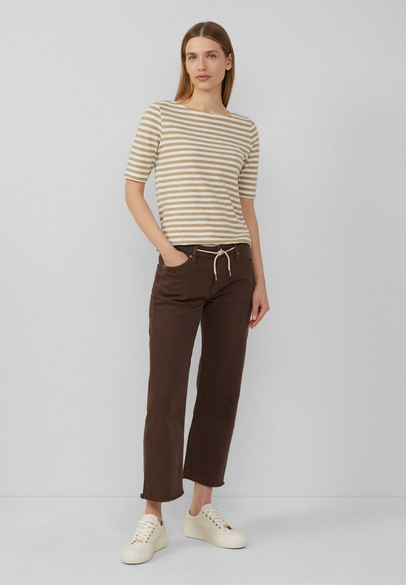 Gestreiftes, beiges und sandfarbenes Kurzarmshirt kombiniert mit braunen, geraden Hosen und cremefarbenen Sneakers. Die Hose hat eine Kordelzugtaillierung.
