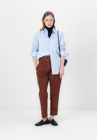 Šviesiai mėlynas marškiniai su kaklaskare, juodas golfas, rudi klostuoti kelnės, juodi slip-on batai ir juoda per petį nešama rankinė. Minimalistinis dizainas, pritaikytas siluetas.