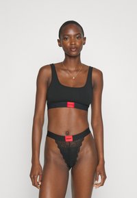 Ensemble de soutien-gorge noir et de string avec un tissu lisse et des bandes de logo rouges ; le string présente des détails en dentelle le long des bords.
