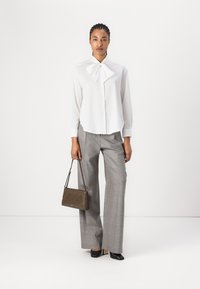 Camicia bianca con bottone e un grande fiocco, pantaloni a righe grigi a gamba larga e una piccola borsa verde oliva con motivo a zigzag. Tacchi neri.