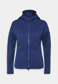 Marinblå huva jacka med en strukturerad diamantmönster, full dragkedja och två sidofickor. Har en logotyp vid fållen och ventilerande tyg.