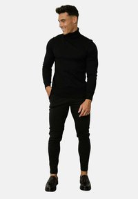 Un pull à col roulé noir avec une texture côtelée, associé à un pantalon noir slim et des mocassins noirs, créant un look monochrome cohérent.