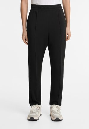 Black sweatpants with a stretchy waistband, featuring vertical seams, made of soft fabric, paired with light-colored sneakers.