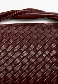 Gewebte Handtasche aus burgunderrotem Leder mit glatter Textur und robustem oberem Griff, rechteckige Form und dezente Nähdetails.