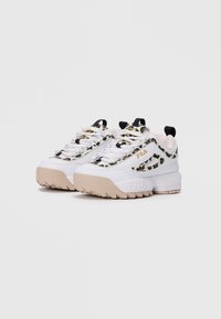 Par bijelih FILA tenisica s bež potplatima i leopard print uzorcima, prikazanih na jednostavnoj svijetlosivoj pozadini.