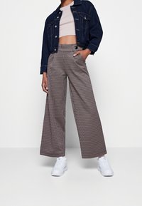 Breda byxor i houndstooth-mönster, med hög midja, två sidfickor och ett lätt tyg. Tillsammans med en denimjacka och vita sneakers.