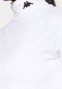 Biały sweter z golfem o dopasowanym kroju, wykonany z miękkiego materiału. Zdobiony czarnym haftowanym logo na kołnierzu.