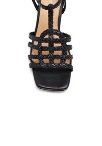 Sandalo in pelle intrecciata nera con punta quadrata e più fasce intrecciate. Presenta una suola testurizzata e un design minimalista.