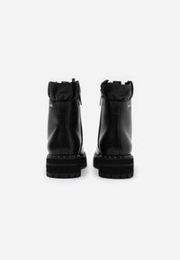 Botas de tobillo de cuero negro con un puño de tela negra texturizada, cremallera lateral y suela gruesa con dibujo, que presenta acentos de tachuelas plateadas.