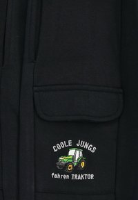 Schwarzer Sweatshirt mit einer Vorderseite Tasche und besticktem Design mit einem grünen Traktor und dem Text "COOLE JUNGS fahren TRAKTOR." Weicher Stoff.