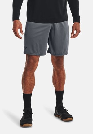 Mand iført grå atletikshorts, sort langærmet trøje, sorte sokker og sorte sportssko, stående på en hvid baggrund.