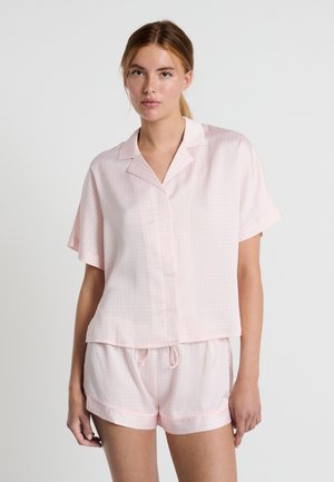 Ensemble de pyjama rose clair comprenant un haut à boutons à manches courtes et un short assorti, tous deux ornés d'un discret motif à pois et avec une taille à cordon ajustable.
