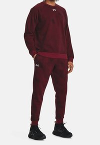 Maroon sweatshirt och sweatpants-set med struktur, rund halsringning, elastiska ärmslut och logotypdetalj. Bärs med svarta träningsskor.
