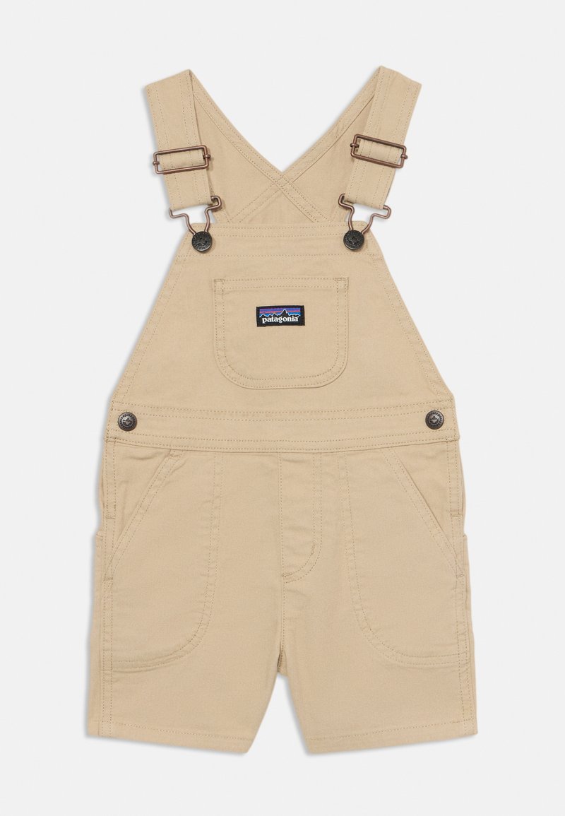 Salopette courte en coton beige avec bretelles réglables, poche poitrine avant et deux poches latérales. Comprend des accessoires en métal et des accents cousus.