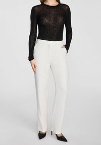 Czarny, długi rękaw, przezroczysty top zestawiony z jasnobeżowymi spodniami o wysokim stanie, charakteryzującymi się gładką fakturą i dopasowanym krojem, uzupełniony czarnymi szpilkami.