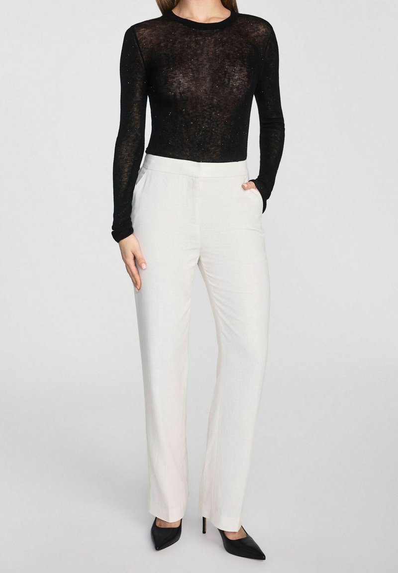 Czarny, długi rękaw, przezroczysty top zestawiony z jasnobeżowymi spodniami o wysokim stanie, charakteryzującymi się gładką fakturą i dopasowanym krojem, uzupełniony czarnymi szpilkami.