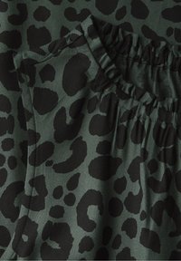 Detailní záběr tmavě zelené látky s černými leopardími skvrnami, s elastickým pasem a viditelným šitím kapes.