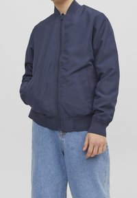 Granatowa kurtka bombowca, lekki materiał, zamek błyskawiczny z przodu, boczne kieszenie, ściągacze na rękawach i u dołu, w połączeniu z jasnoniebieskimi dżinsami.