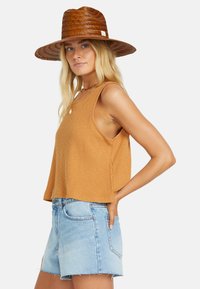 Hnedastočervený rebrovaný crop top s širokými ramienkami, skombinovaný s svetlomodrými džínsovými šortkami s rozstrapkanými okrajmi. Doplní ho tkaný slamenný klobúk.