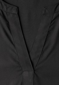 Gros plan sur un tissu noir avec un détail d'encolure en V cousu et des lignes de couture nettes et précises.