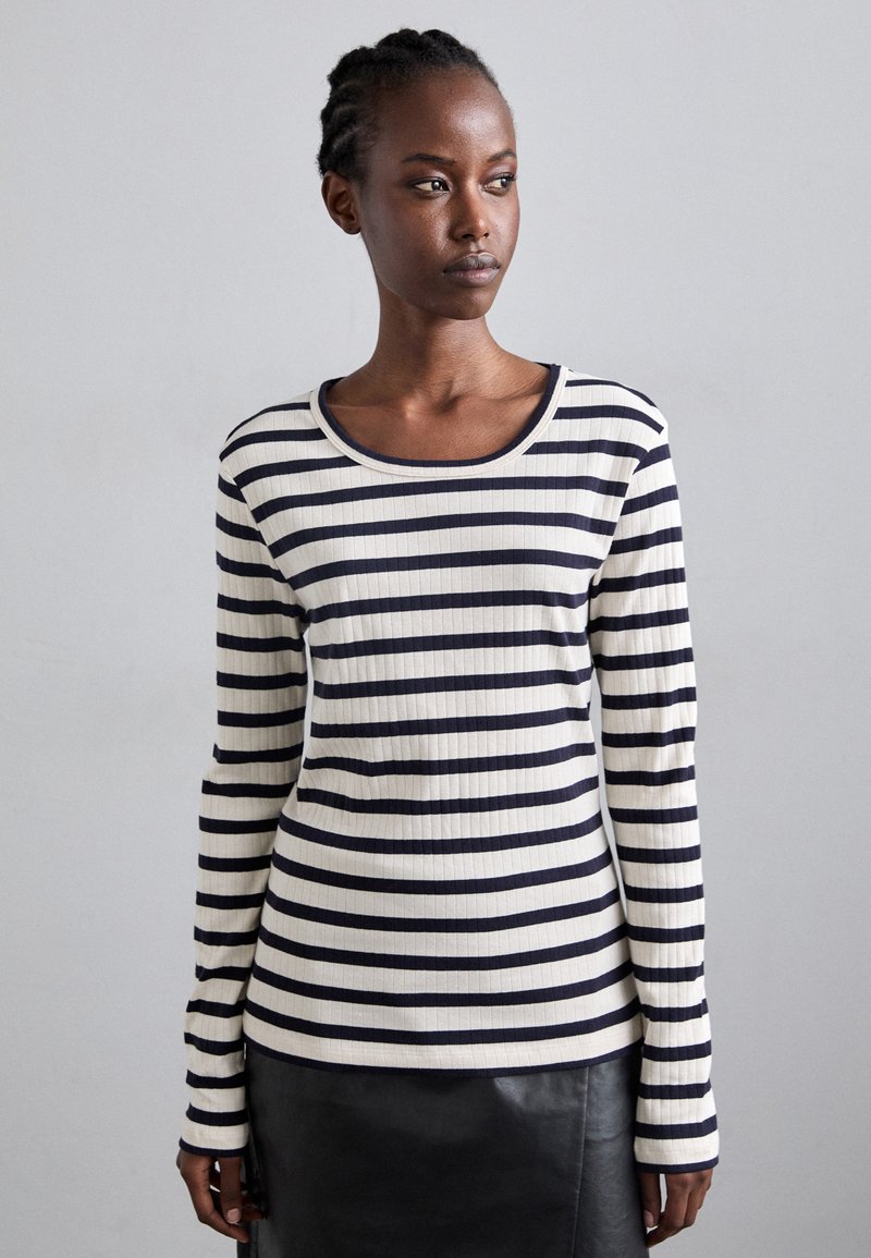 Striped long-sleeve top in cream and navy, ribbed texture, rounded neckline, fitted silhouette, with a slightly longer waist and cuffs.