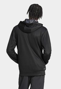 Svart huvtröja med en slät textur, med en kontrasterande inre huva i grått med ett subtilt mönster, långa ärmar och ribbat avslut.