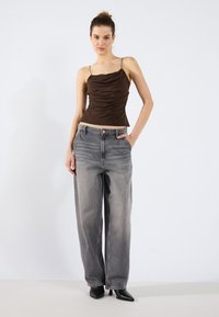 Bruine, aansluitende, gerimpelde tanktop met spaghettibandjes, gecombineerd met losse, vervaagde grijze jeans en zwarte puntige hakken. Eenvoudig ontwerp, casual uitstraling.