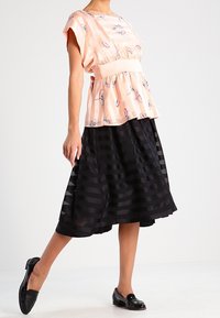 Top de estampado de melocotón con mangas cortas, combinado con una falda negra de pliegues con rayas horizontales. Mocasines negros completan el conjunto.