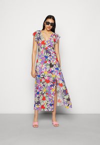 Vestido floral envolvente com mangas bufantes, fundo roxo, decorado com margaridas e corações brilhantes, detalhe de fenda, combinado com mules rosa e óculos de sol.