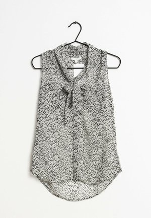 Blouse sans manches avec imprimé léopard noir et blanc, détail à nouer au col, suspendue sur un cintre noir sur fond blanc.