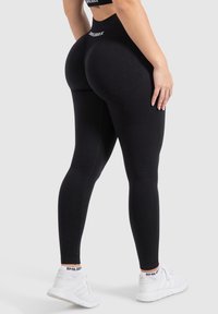 Leggings sportivi neri con vita alta, caratterizzati da un design texturizzato e cuciture a contrasto. Abbinati a scarpe da ginnastica bianche.