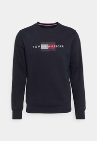 Felpa blu navy in misto cotone, con collo a giro, maniche lunghe e un design logo frontale con strisce orizzontali in rosso e bianco.