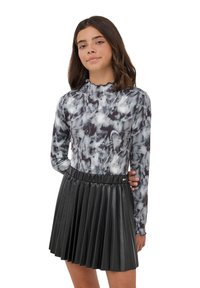 Maglietta a maniche lunghe con motivo marmorizzato in bianco e nero abbinata a una gonna plissettata in similpelle nera, con vita solida e accessori in metallo.