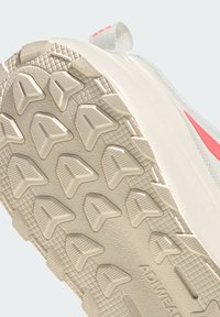 Primer plano de la suela beige de una zapatilla con patrón triangular en la banda de rodadura y agarre texturizado, mostrando parte del lateral superior blanco y rosa.