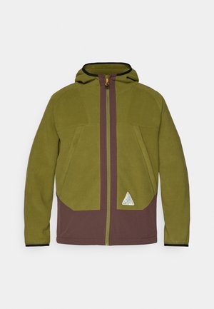 Olíva zöld és barna színű polár dzseki kapucnival, elöl cipzárral és háromszöglogóval a szegélyen. Az anyag texturált.