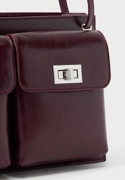Σκούρο δερμάτινο χιαστί τσάντα σε μπορντό χρώμα με μπροστινή θήκη με καπάκι ασφαλισμένη με ορθογώνιο κούμπωμα σε ασημί τόνο.