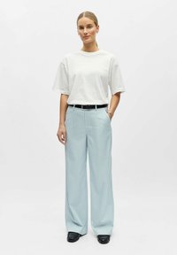 Valge lühikeste varrukatega t-särk kombineerituna helesiniste vertikaalsete triibuliste laiade pükstega. Must vöö ja läikivad mustad kingad täiustavad välimust.