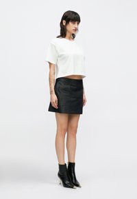 Biały krótki t-shirt w zestawieniu z ciemną mini spódnicą dżinsową i czarnymi skórzanymi botkami z złotymi detalami.