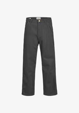 Persona vistiendo una sudadera con capucha y cremallera azul marino, camiseta gráfica blanca, pantalones oscuros holgados y zapatillas blancas con suelas de goma, de pie contra un fondo liso.