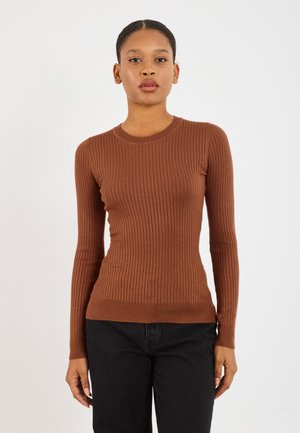 Pull à manches longues côtelé marron avec un col rond. Doté d'une coupe slim et d'un tissu texturé. Associé à un jean foncé, mains visibles sur les côtés.