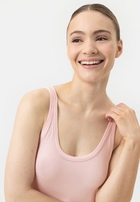 Haut sans manches rose clair avec un décolleté arrondi, texture lisse et détails de couture subtils, porté par une personne sur un fond neutre.