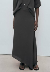 Larga y fluida falda gris oscuro con una hendidura lateral, hecha de tela suave. Combinada con una camiseta holgada gris oscuro y sandalias planas.