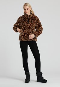 Leopardmønstret fleece-pullover med lynlås foran, kontrastfarvet sort krave og løst fit. Sammen med sorte leggings og ankelstøvler.