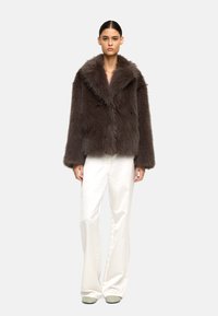 Brązowa kurtka z sztucznego futra z szalowym kołnierzem, o luźnym kroju i długich rękawach, zestawiona z białymi szerokimi spodniami.