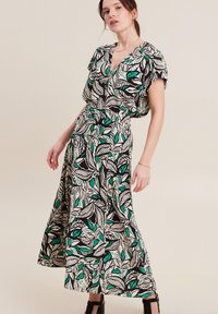 Robe maxi avec un motif audacieux de feuilles vertes et noires sur un fond crème, dotée d'un décolleté en V et de manches courtes et amples.