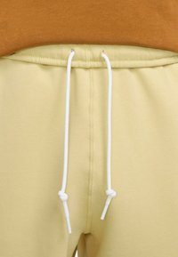Pantaloni sportivi galbeni cu talie ajustabilă, având șnururi albe și o textură moale. Talie are un finisaj neted și un detaliu subtil de cusătură.