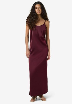 Vestido largo de satén burdeos con tirantes finos, textura suave y corte holgado, que llega por debajo de los tobillos, combinado con zapatos de tacón abierto.